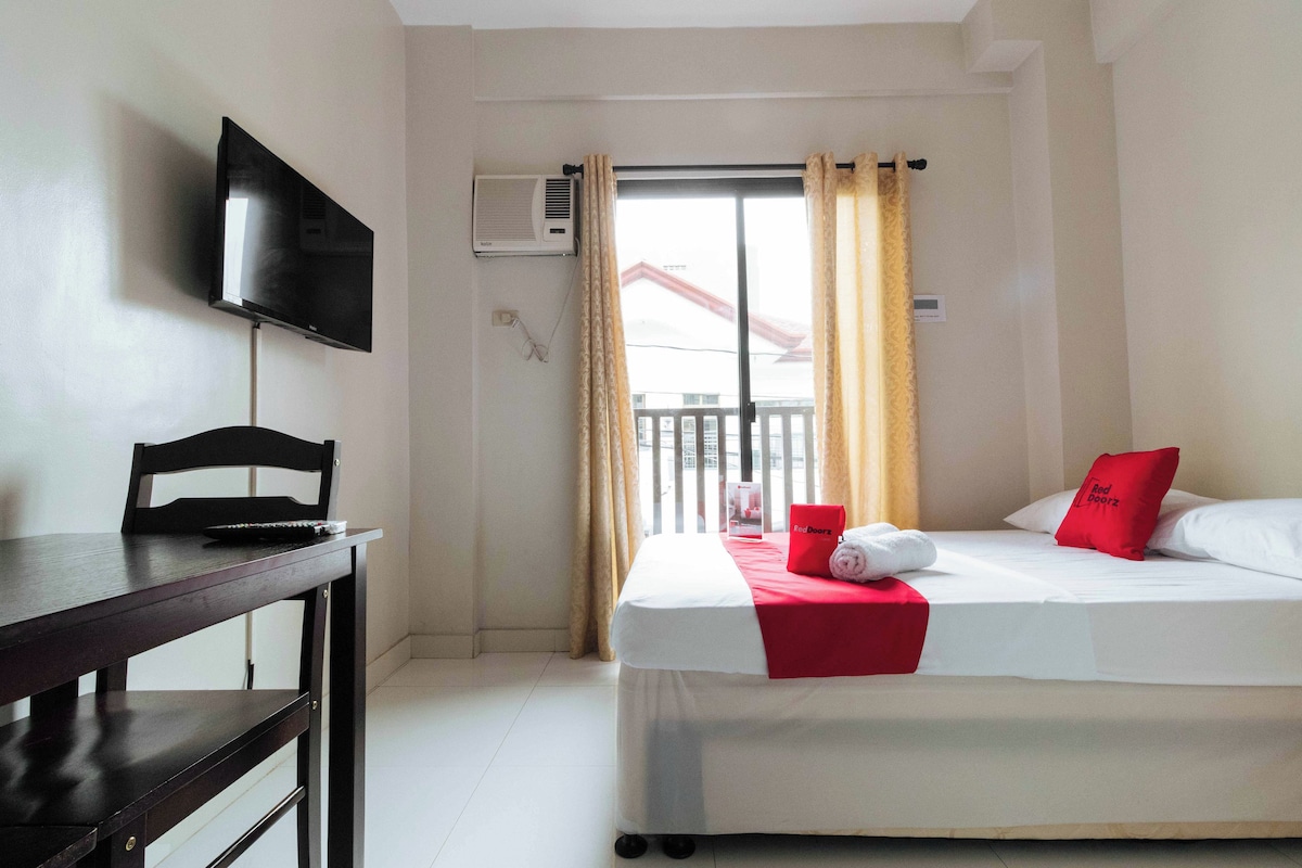 A hotel room with a bed, a desk, a chair, a TV, an air conditioner, and a window with curtains.