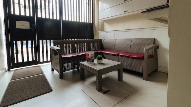 A room with a sofa, a small table with a plant, a bench, and a door with a sign. - RedDoorz near NAIA Terminal 1 (Parañaque)