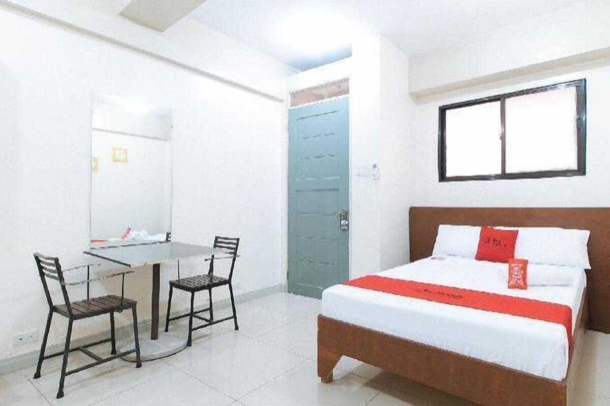A room with a bed, a desk with chairs, a window, and a door.