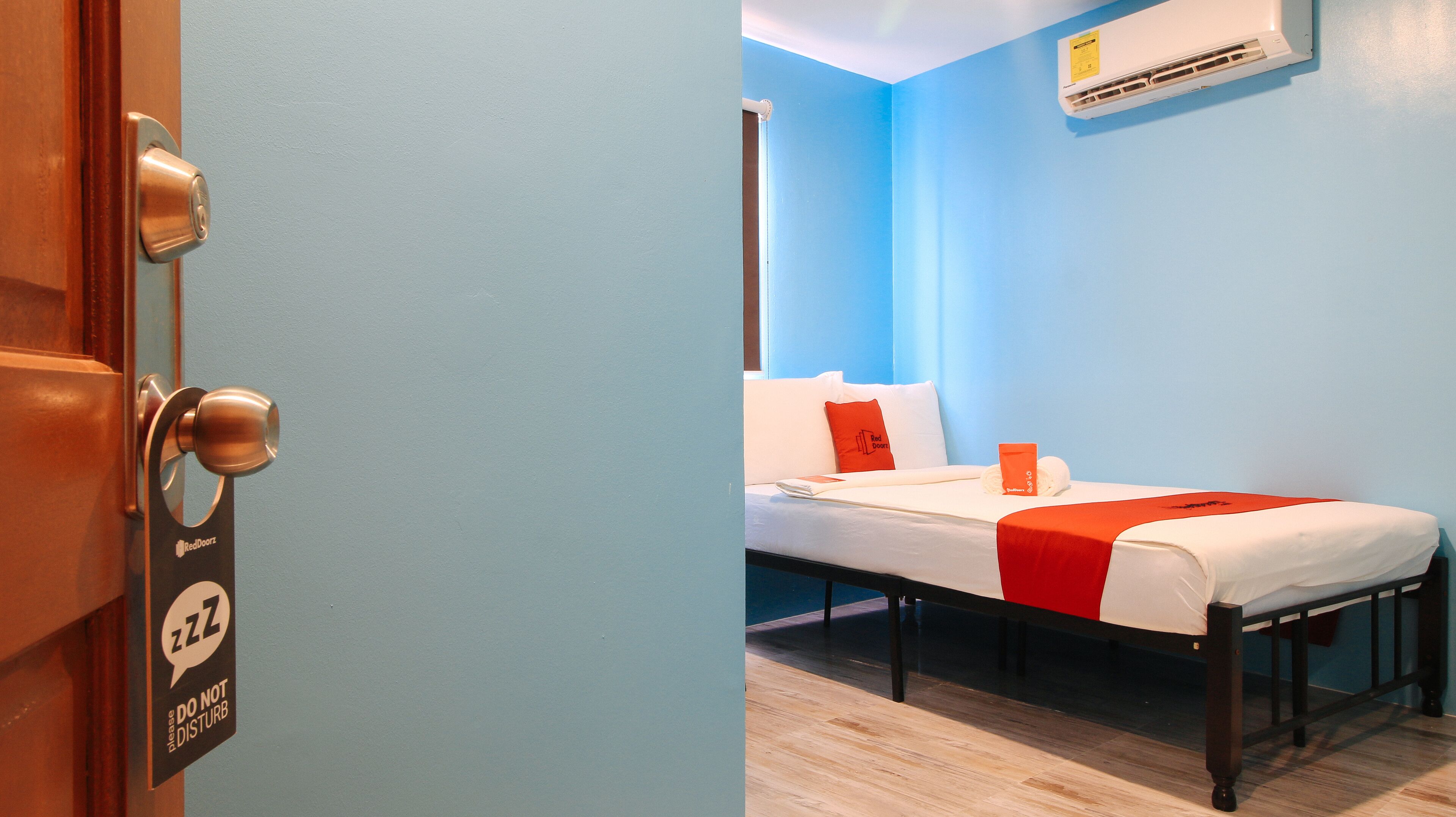 A hotel room with a bed, a bedside table, a nightstand, a window, and an air conditioning unit.