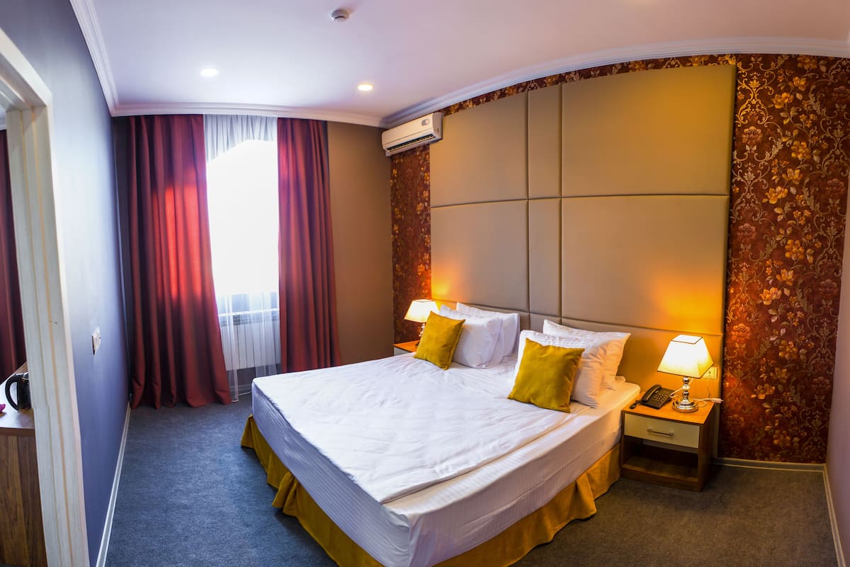 A hotel room with a large bed, two bedside lamps, a nightstand, and a decorative wall panel.