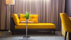 Una habitación moderna con un sofá amarillo, una mesita redonda con una planta, una lámpara de pie y una silla amarilla.
