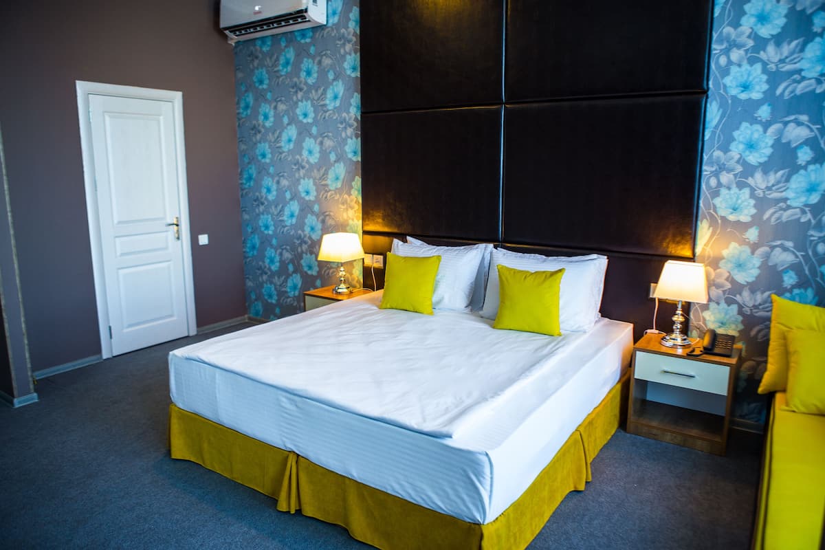 A hotel room with a large bed, two bedside tables with lamps, floral wallpaper, and a door.