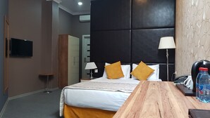 Una habitación de hotel con una cama, mesitas de noche, un escritorio, una lámpara, una botella de agua y un teléfono.