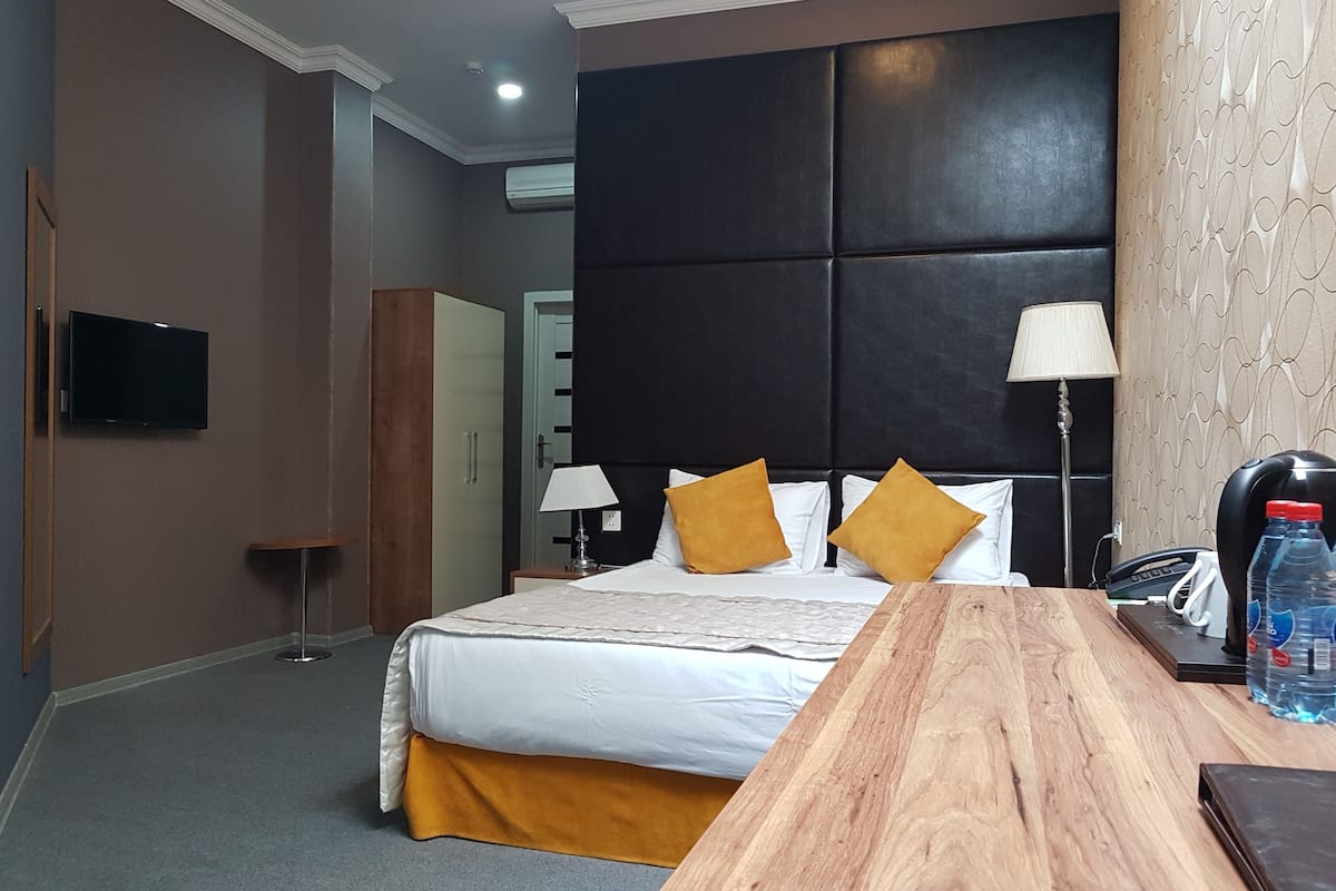 A hotel room with a bed, bedside tables, a desk, a lamp, a water bottle, and a phone.