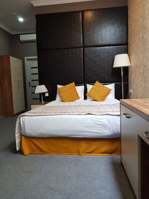 A hotel room with a large bed, a bedside table, a lamp, and a wardrobe.