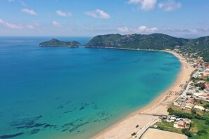 Un pueblo costero con una playa, edificios y colinas al fondo.