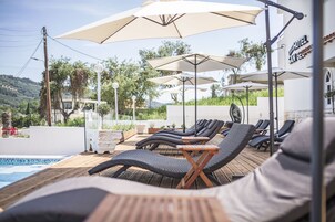 Un área junto a la piscina con sillones de descanso y sombrillas, una piscina y vistas del paisaje circundante.