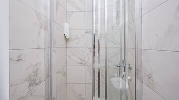 A glass-enclosed shower stall with marble tiles and a handheld showerhead.
