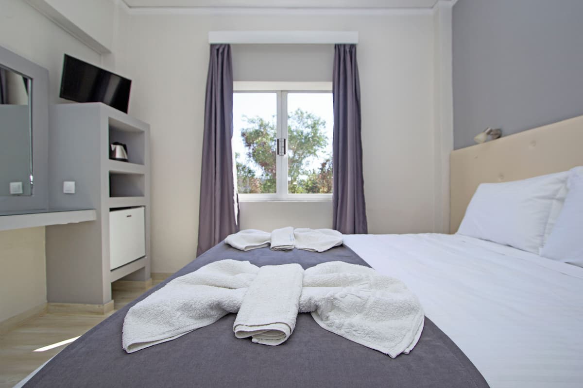 Habitación de hotel con una cama, un televisor en un estante y una ventana con cortinas.