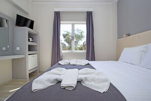 A hotel room with a bed, a TV on a shelf, and a window with curtains.