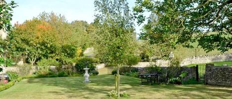 A well-maintained garden with a stone wall, a fountain, and a table and chairs set up for outdoor dining.