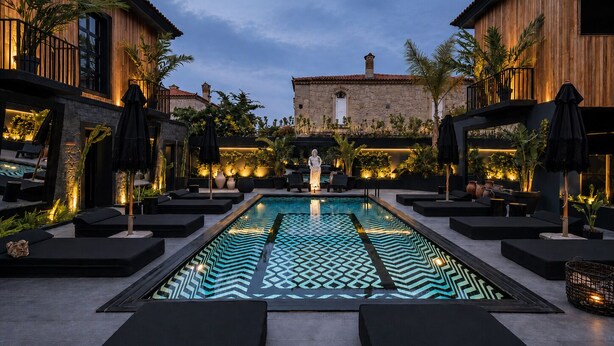 A pool area with lounge chairs, a statue, and a stone building in the background. - The Local House Alaçatı (Cesme)