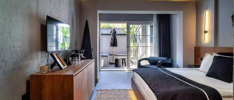 A modern hotel room with a large bed, a wooden dresser, a flat-screen TV, and a view of the outdoors.