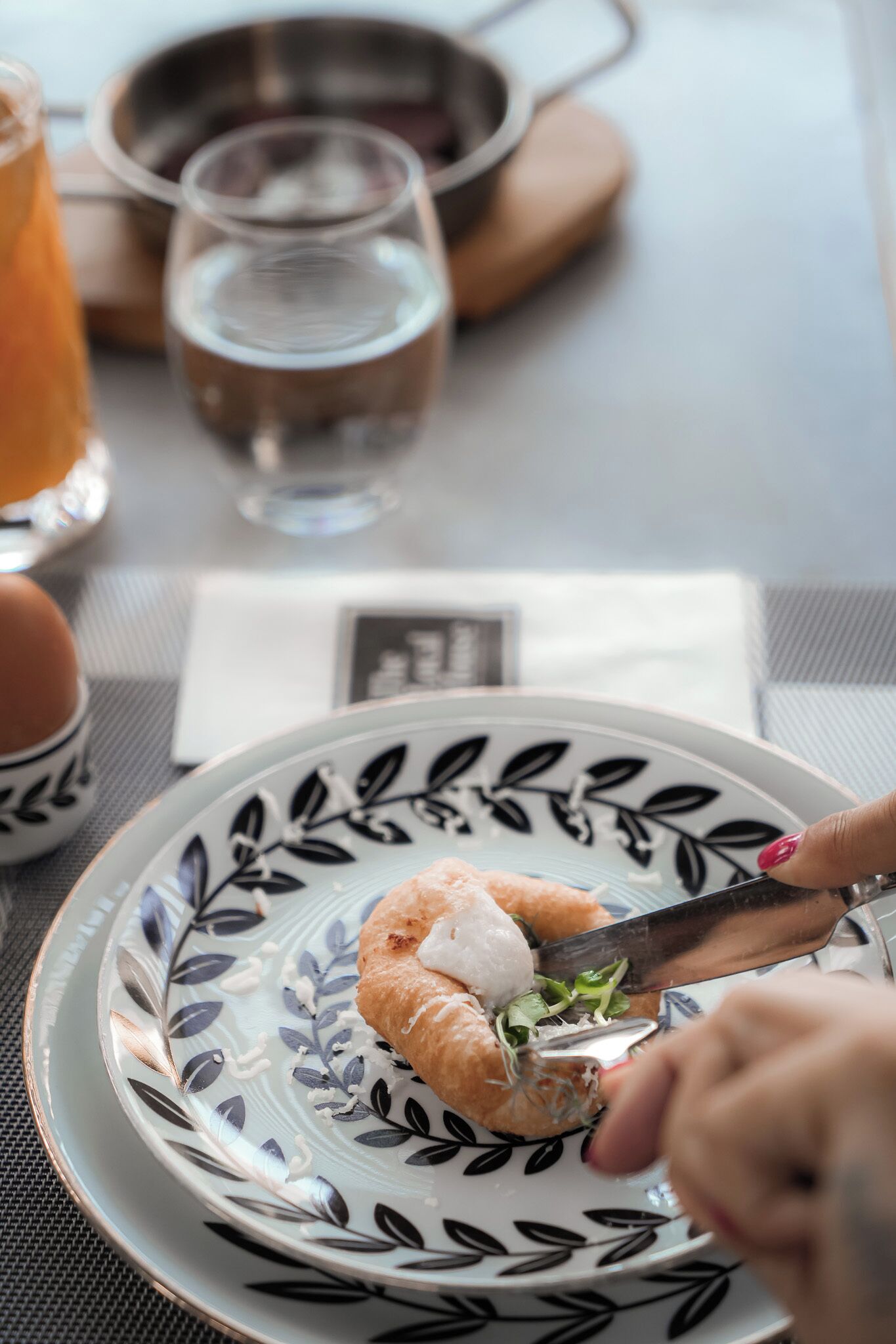 Une assiette avec un croissant et un couteau qui le coupe, un verre d’eau et une tasse de thé sur une table.