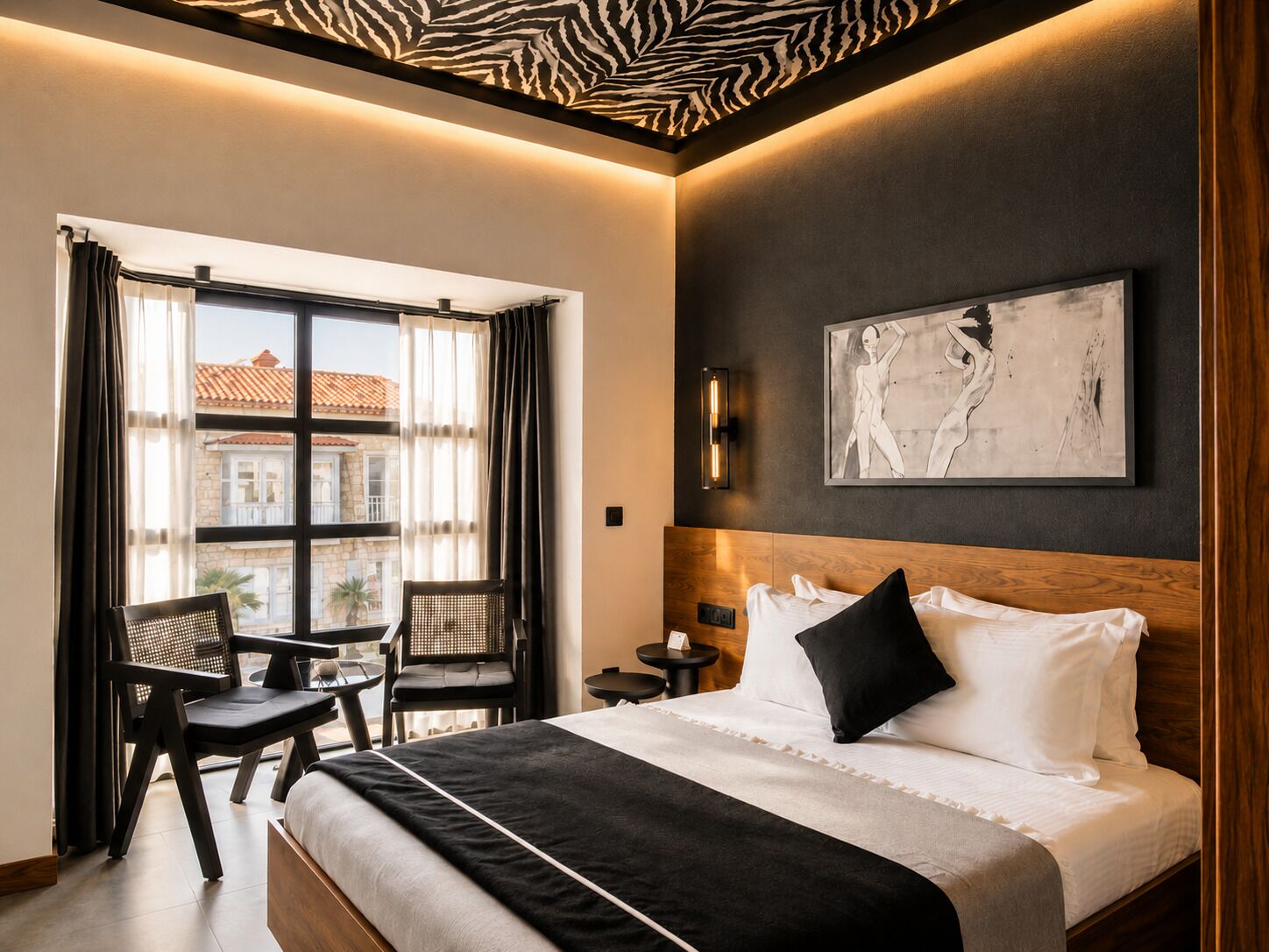 A modern hotel room with a large bed, a small table, two chairs, a view of buildings outside, and a zebra-patterned ceiling.