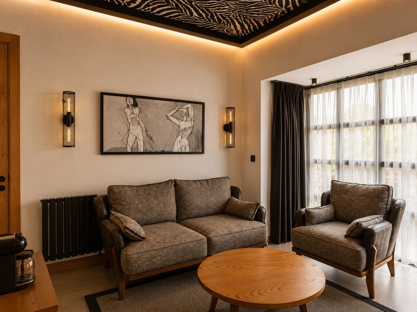 Una sala de estar moderna con un sofá, un sillón y una mesita de centro redonda. Hay una obra de arte grande con marco en la pared y un radiador debajo del sofá.