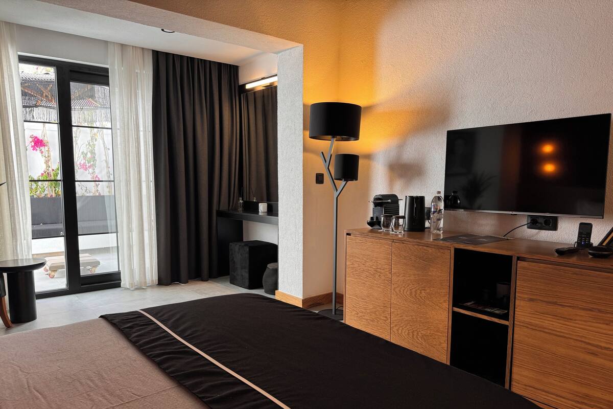 A modern hotel room with a large bed, a flat-screen TV, a coffee machine, and a desk with a lamp.