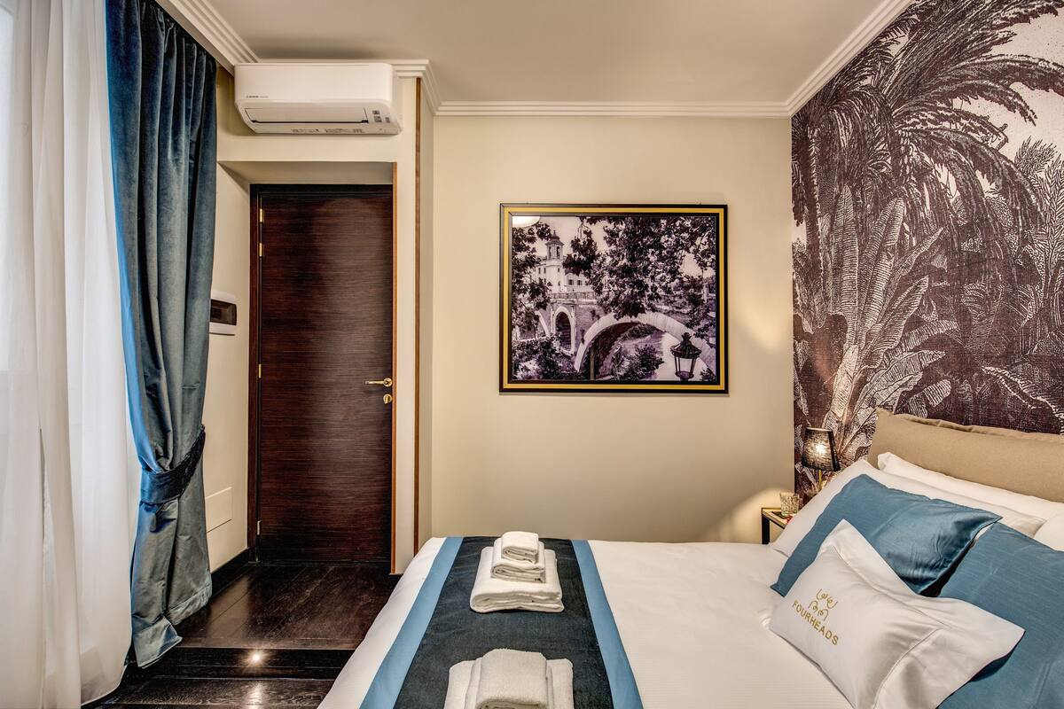 A hotel room with a bed, a framed picture, a nightstand, and a door.