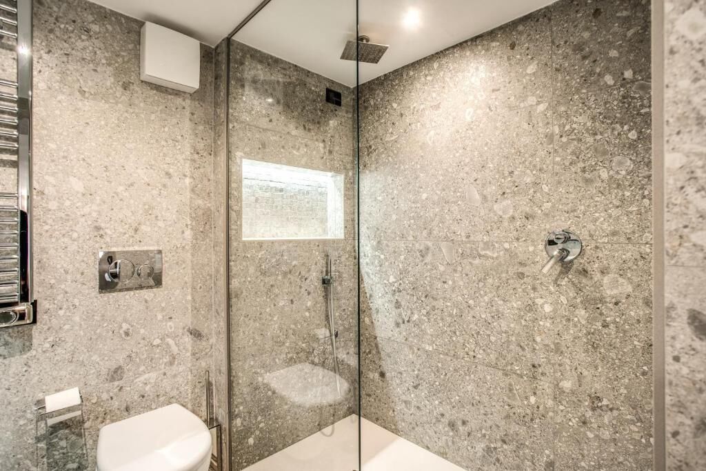A modern bathroom with a glass-enclosed shower, a white toilet, and a marble wall.