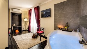 A modern bathroom with a large bathtub, a vanity with a mirror, a television on the wall, and a red chair. - PAX Hotel (Rome)