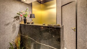A modern bathroom with a marble vanity, a gold mirror, and a black door. - PAX Hotel (Rome)
