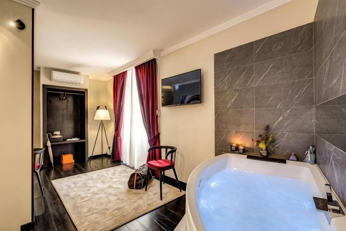 A bathroom with a bathtub, a mirror, a TV, and a red chair.
