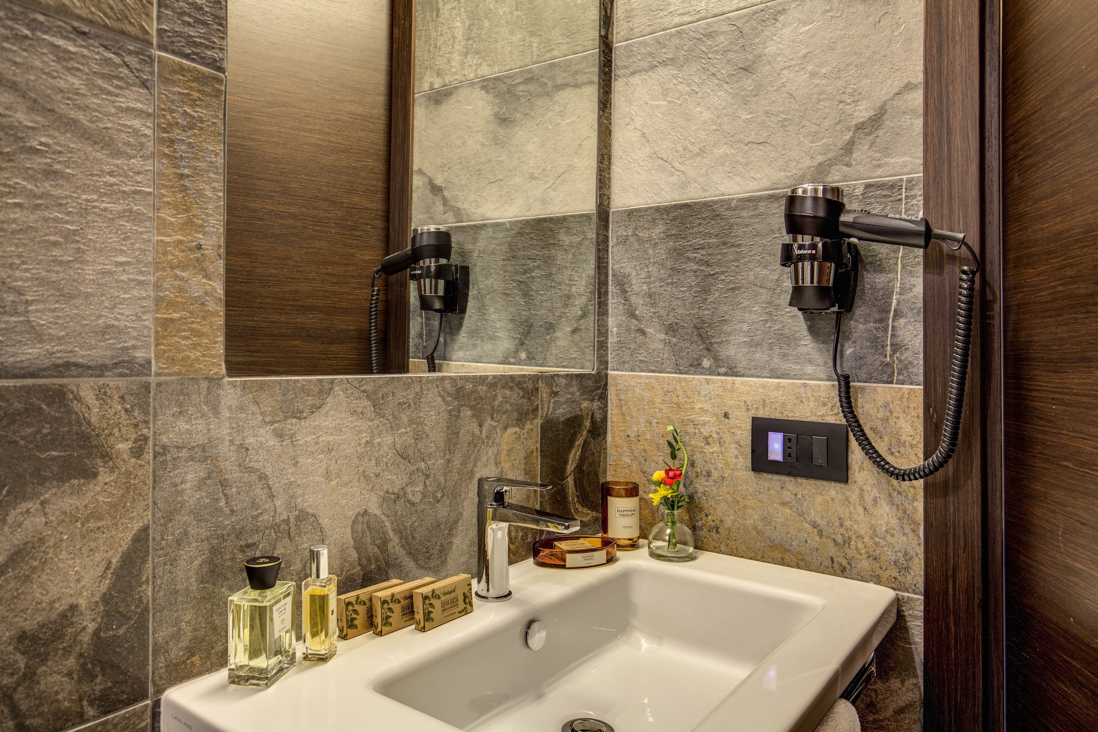 A bathroom with a white sink, two hair dryers mounted on the wall, and a selection of toiletries on the counter.