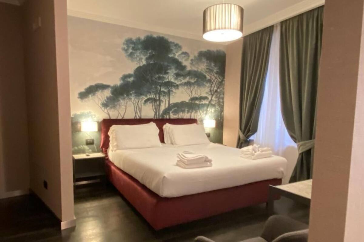 A hotel room with a bed, a nightstand, a chair, and a wall mural.