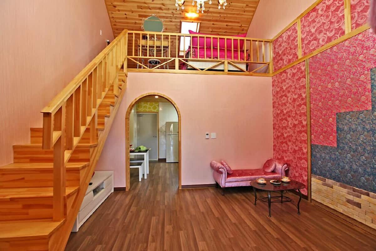 Una habitación amplia con una escalera de madera, un sofá rosa y un comedor.