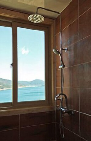 A bathroom with a shower, a window, and a view of the sea.
