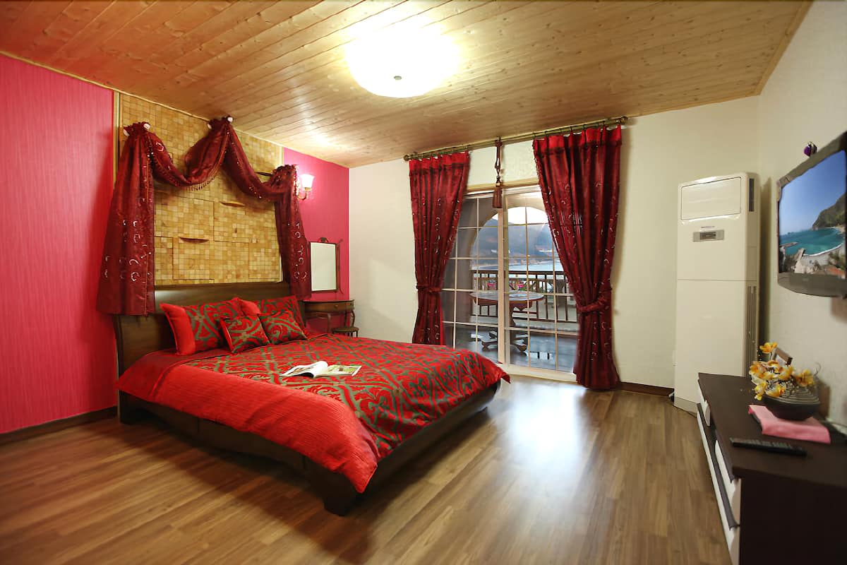 Un dormitorio con una cama grande, cortinas rojas, techo de madera y vistas al mar a través de una ventana.