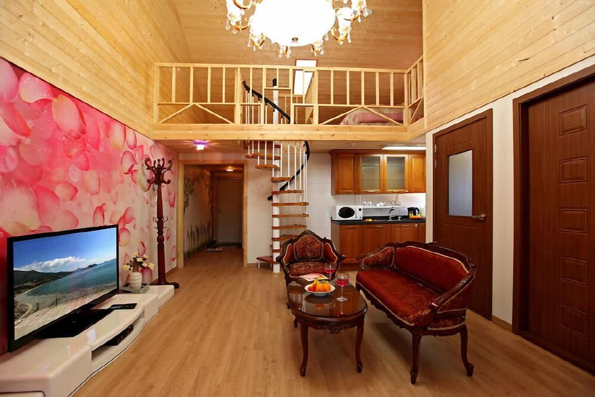 Interior de madera con televisor, dos sillas, una mesa y una escalera que lleva a un altillo.