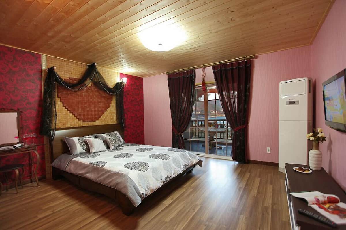 Un dormitorio con techo de madera, una cama con ropa de cama estampada, un escritorio con lámpara y un televisor en la pared.