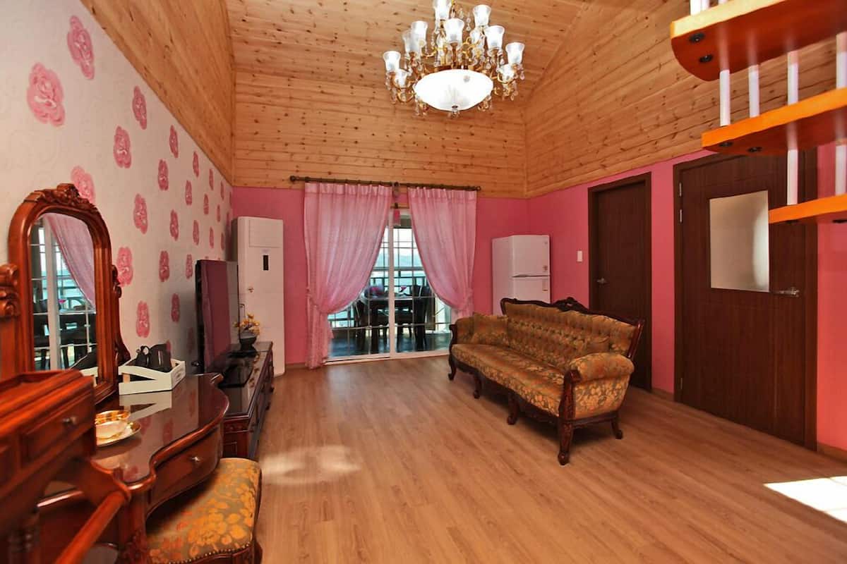 Una habitación con piso de madera, un candelabro, un sofá, un espejo y cortinas rosadas.