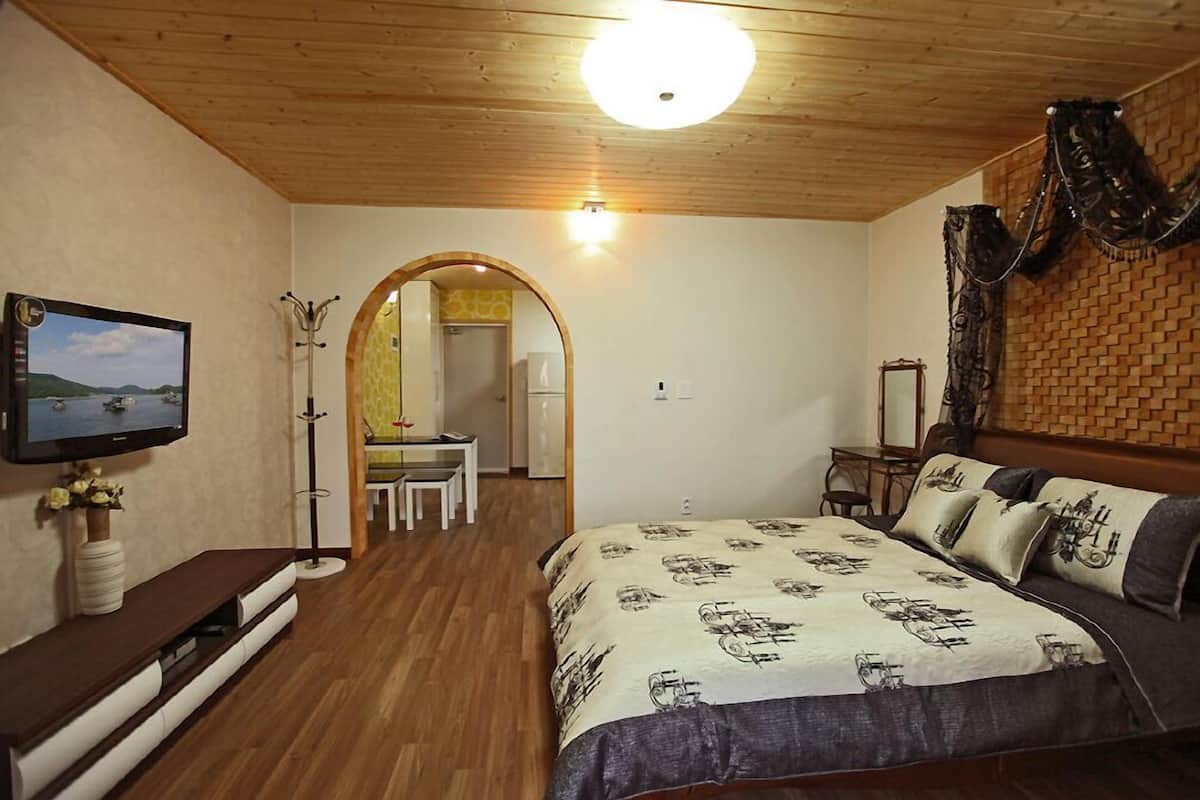 Un dormitorio con techo de madera, una cama con ropa de cama estampada, un televisor en la pared y un espejo en la pared opuesta.