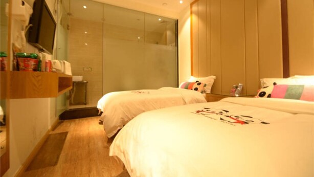 Quarto de hotel com duas camas, um guarda-roupa de madeira, um espelho e cabine de chuveiro em vidro.