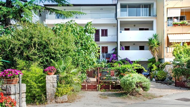 Un immeuble résidentiel doté de nombreux balcons, d’une entrée sécurisée et de divers pots de plantes.
