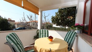 Un balcon avec une table ronde, des chaises à rayures vertes, une nappe jaune et des plantes en pot.