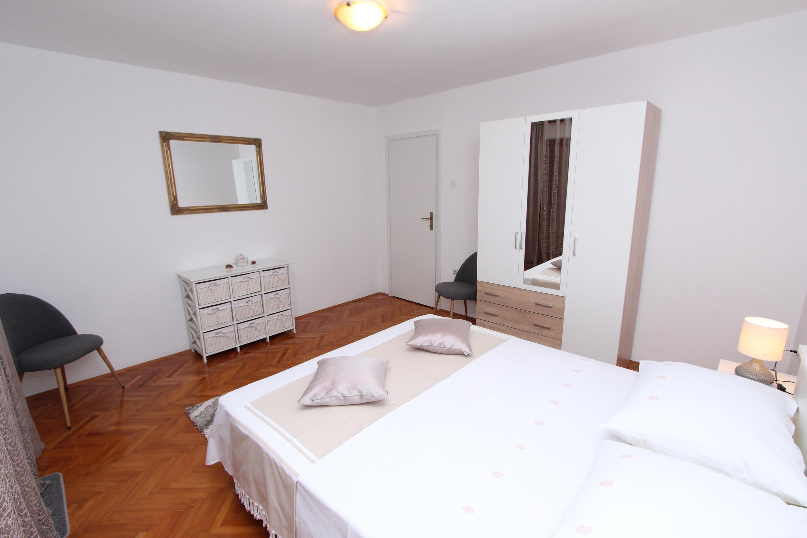 A bedroom with a bed, a dresser, a chair, a mirror, and a wardrobe.