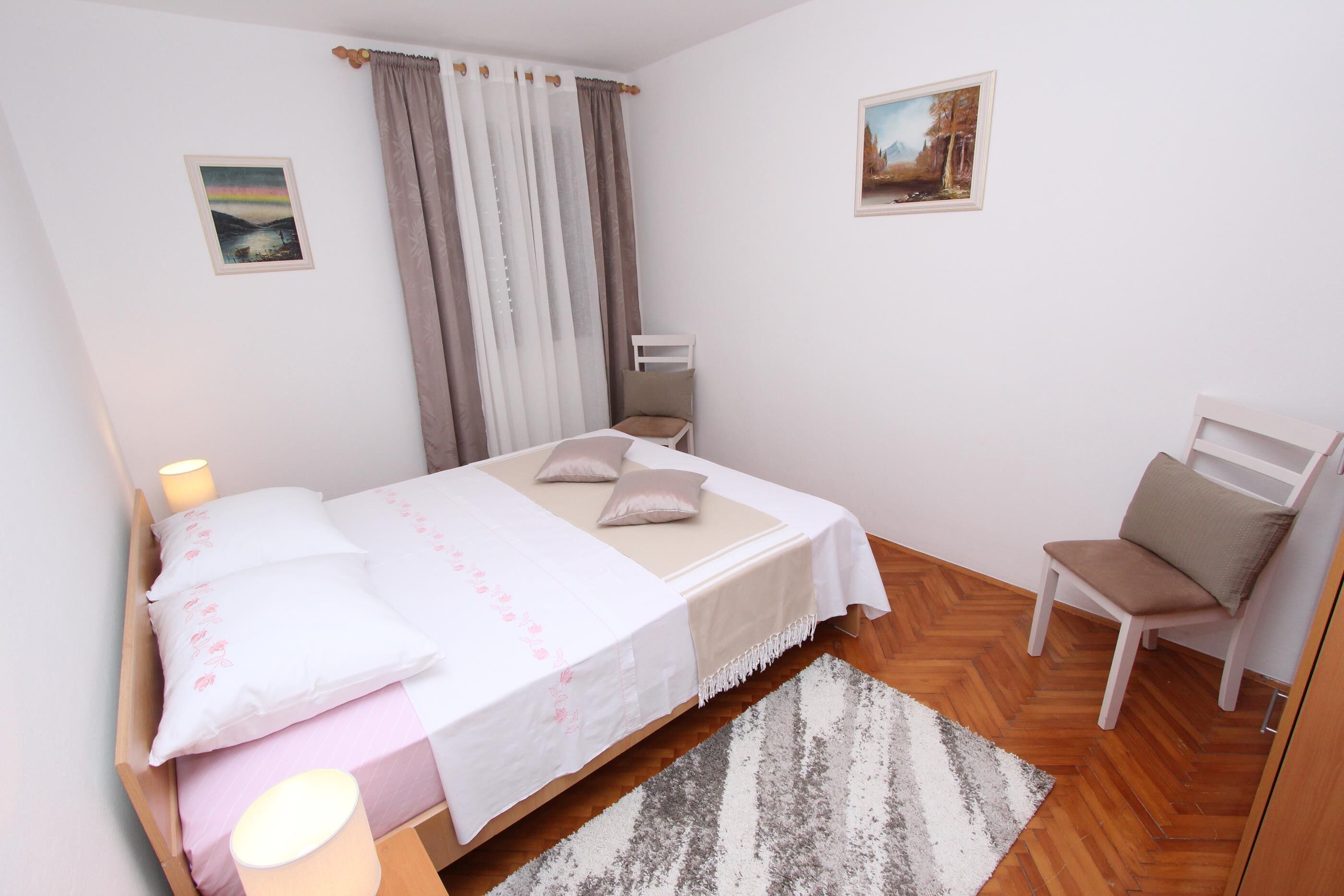 A bedroom with a bed, a chair, a rug, and two paintings on the walls.
