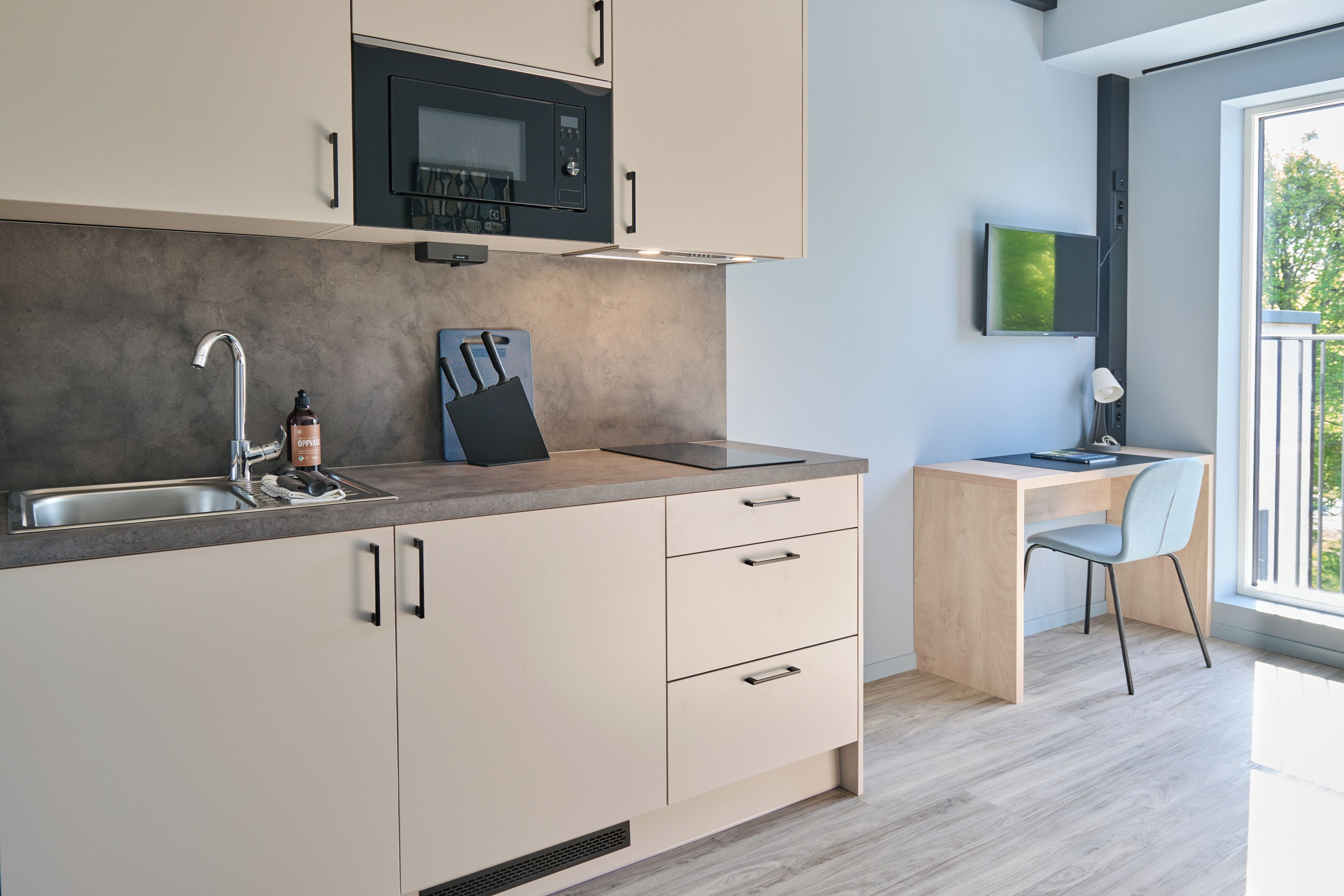 Una cocina moderna con microondas integrado, un lavabo y un escritorio de madera con una silla.