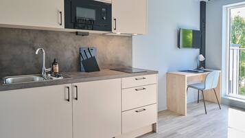 Una cocina moderna con microondas integrado, un lavabo y un escritorio de madera con una silla.