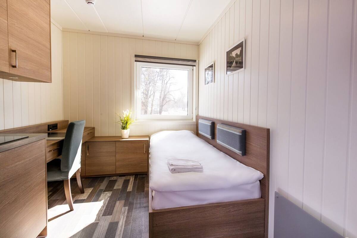 Een kleine slaapkamer met een bed, bureau en stoel.