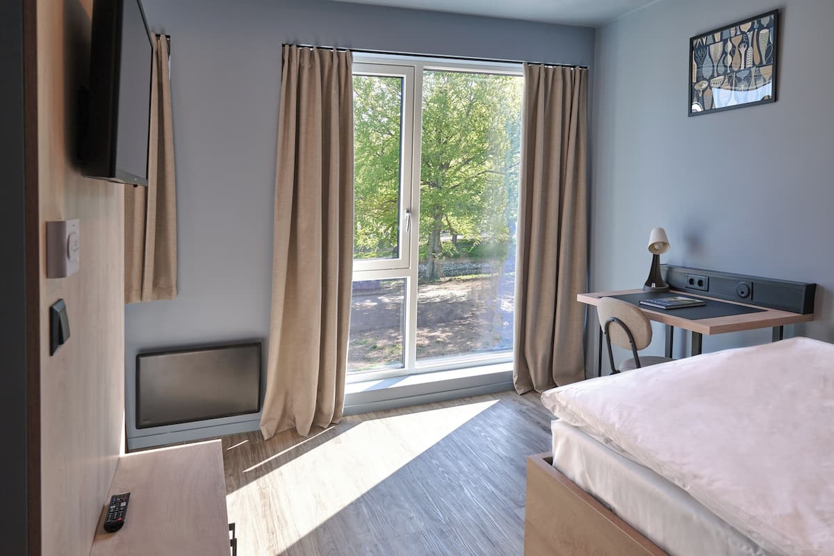 Een hotelkamer met een bed, een bureau met stoel, een televisie en een raam met gordijnen.