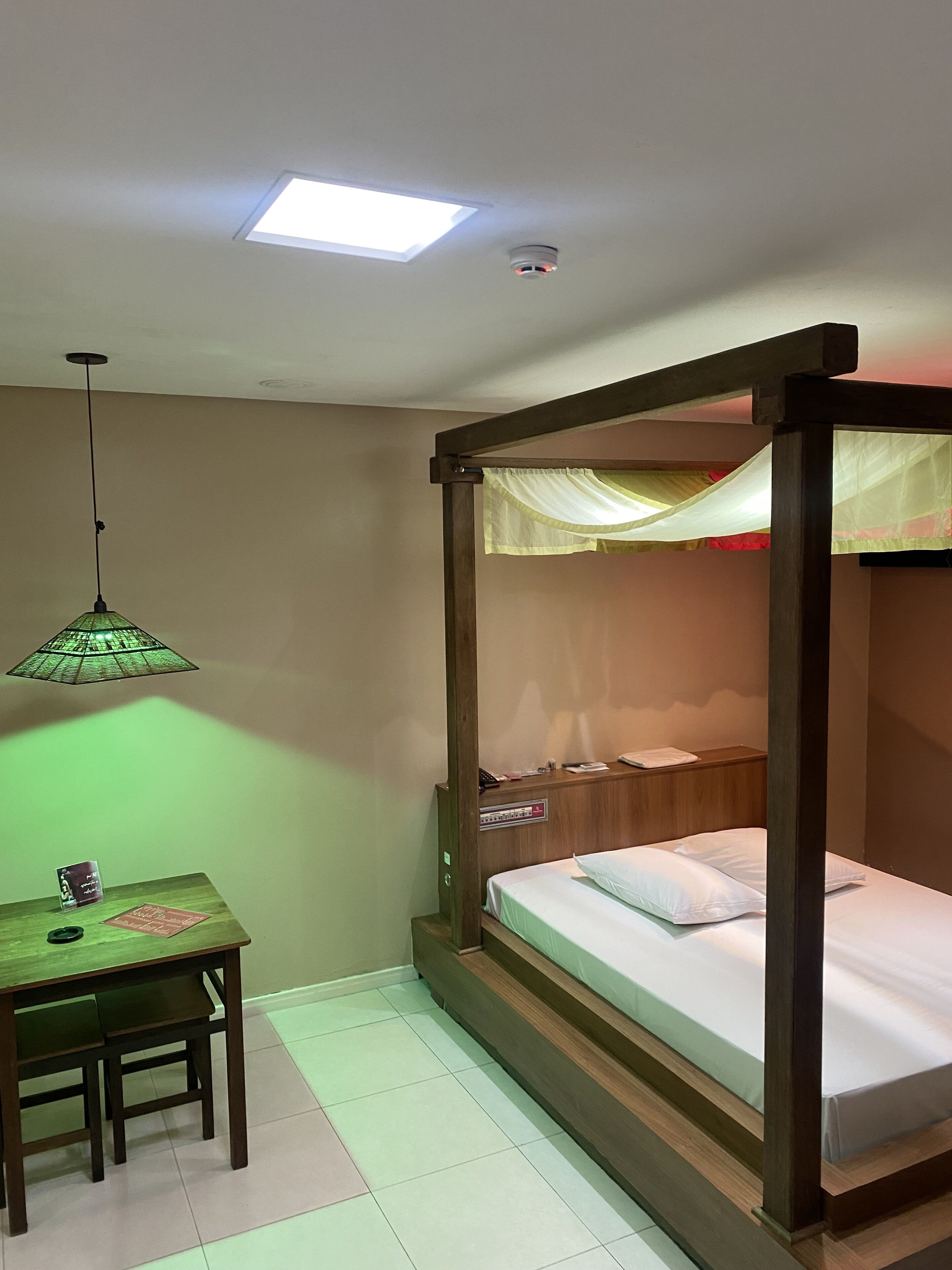 A room with a bunk bed, a desk with a chair, a green table lamp, and a ceiling light.