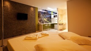 Een hotelkamer met een bed, een aan de muur bevestigde televisie, een kitchenette en een badkamer.