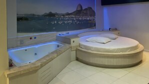 Een moderne badkamer met een ruime badkuip, een aparte douche en een rond zitgedeelte met uitzicht op een stadsbeeld.
