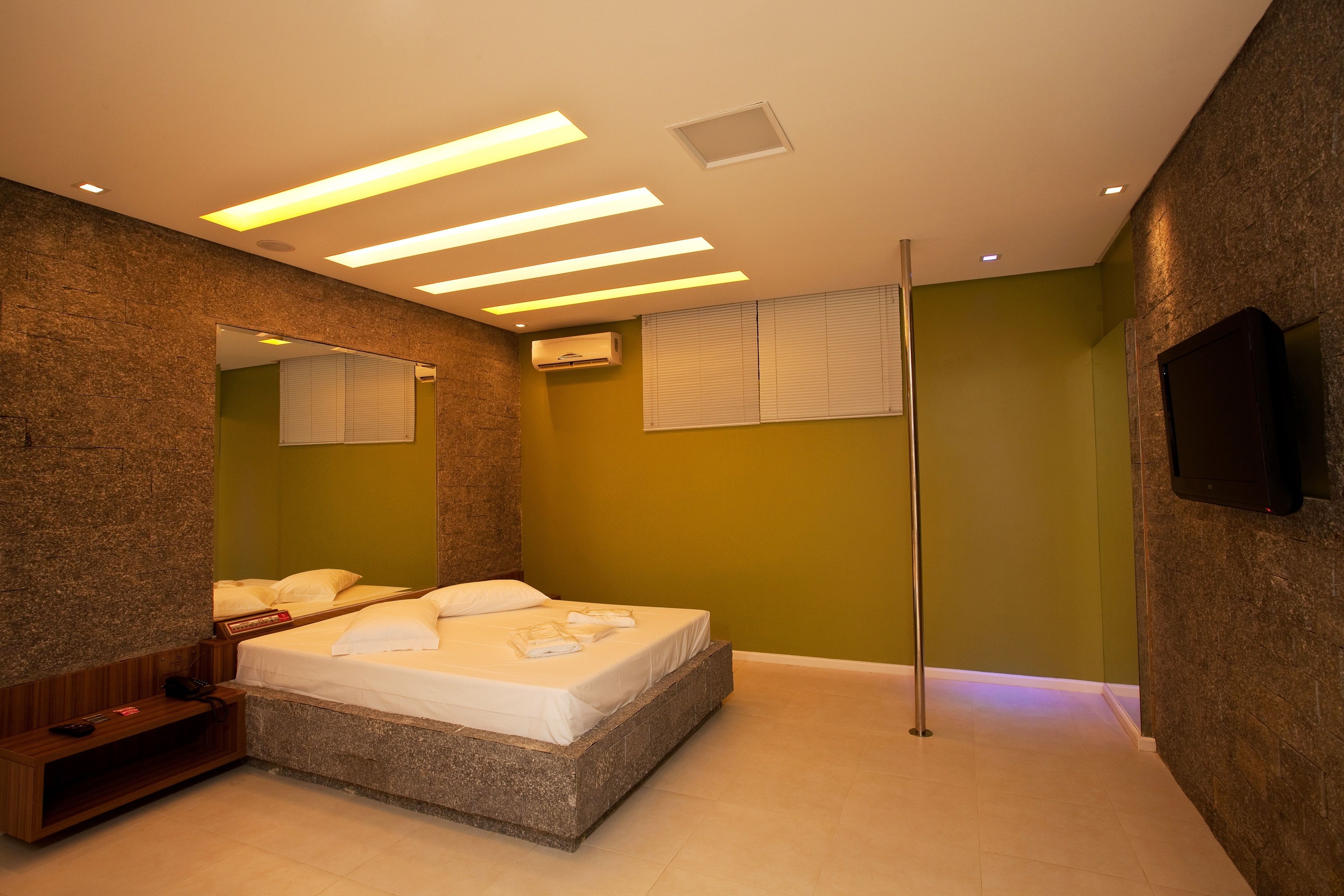 Quarto moderno com uma cama grande, um espelho, televisão de tela plana e abajur.