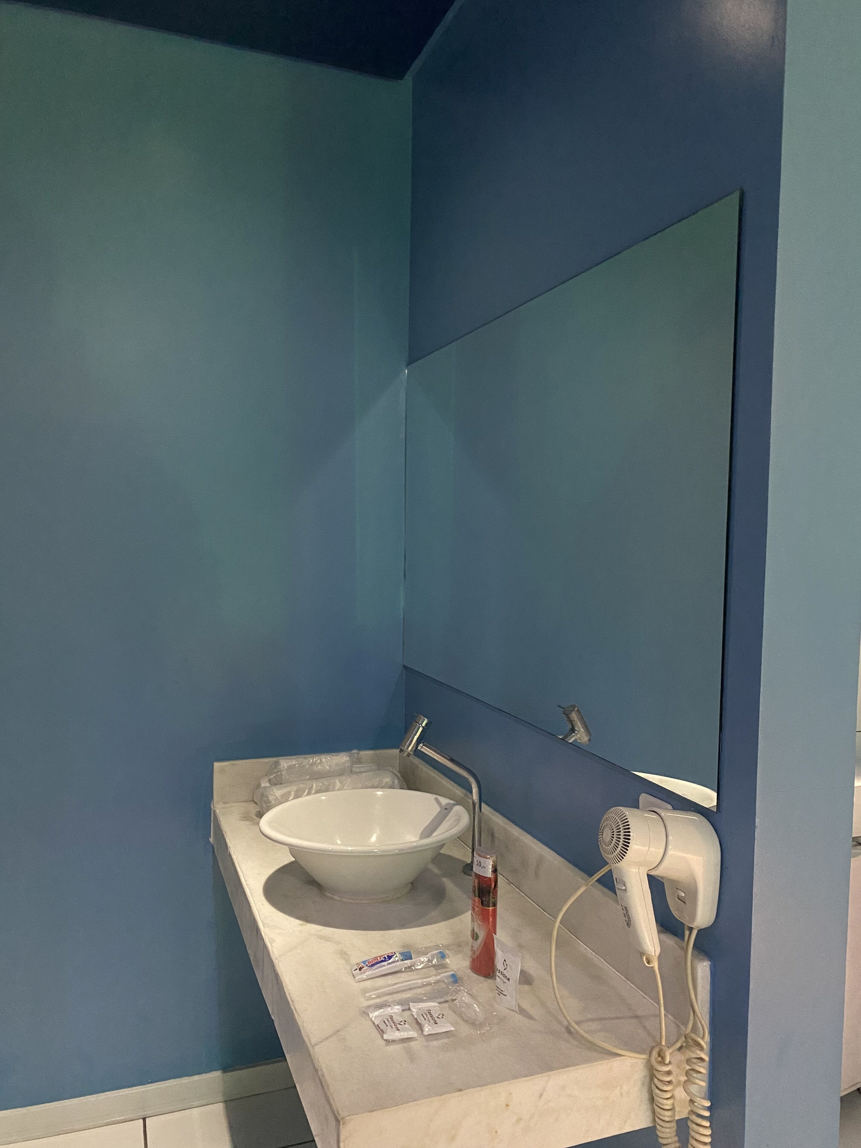 A bathroom with a white sink, blue walls, a mirror, and a hairdryer on the counter.